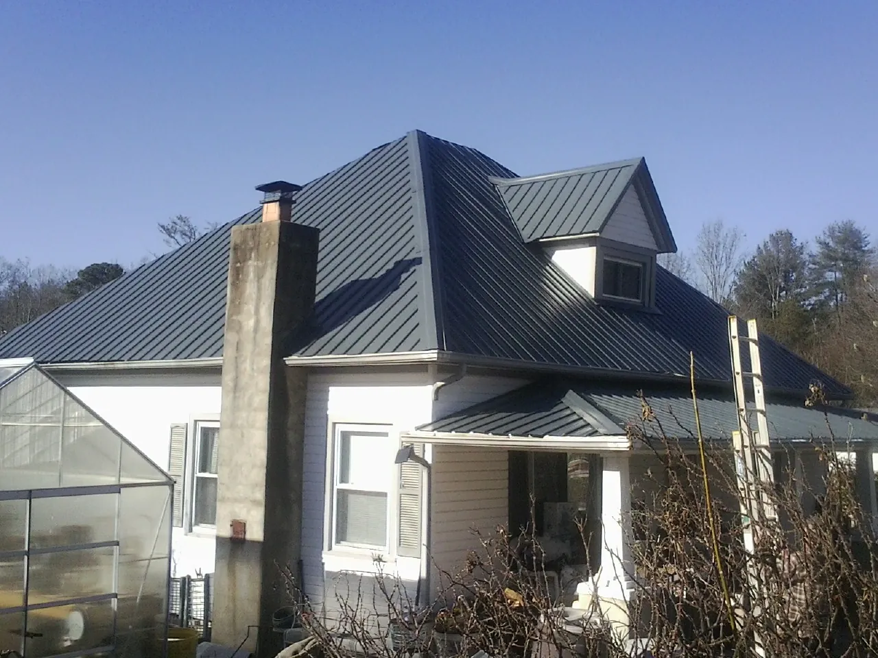 Dark blue standing seam metal roof on a white farmhouse with dormer — Slate & Tile Roof Repair by Roofing Brothers in Interlachen