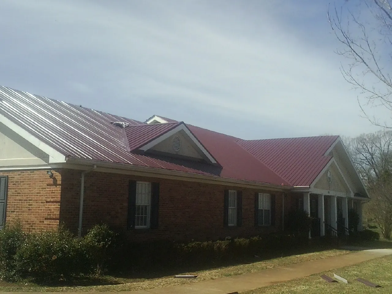 Red metal roof with gabled entries on a long brick building, from a Hail Damage Roof Repair job in Interlachen