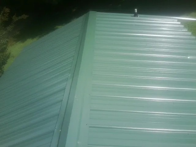 New green metal panels meeting at the ridge of a roof — Flat Roof Repair work by our crew in Interlachen