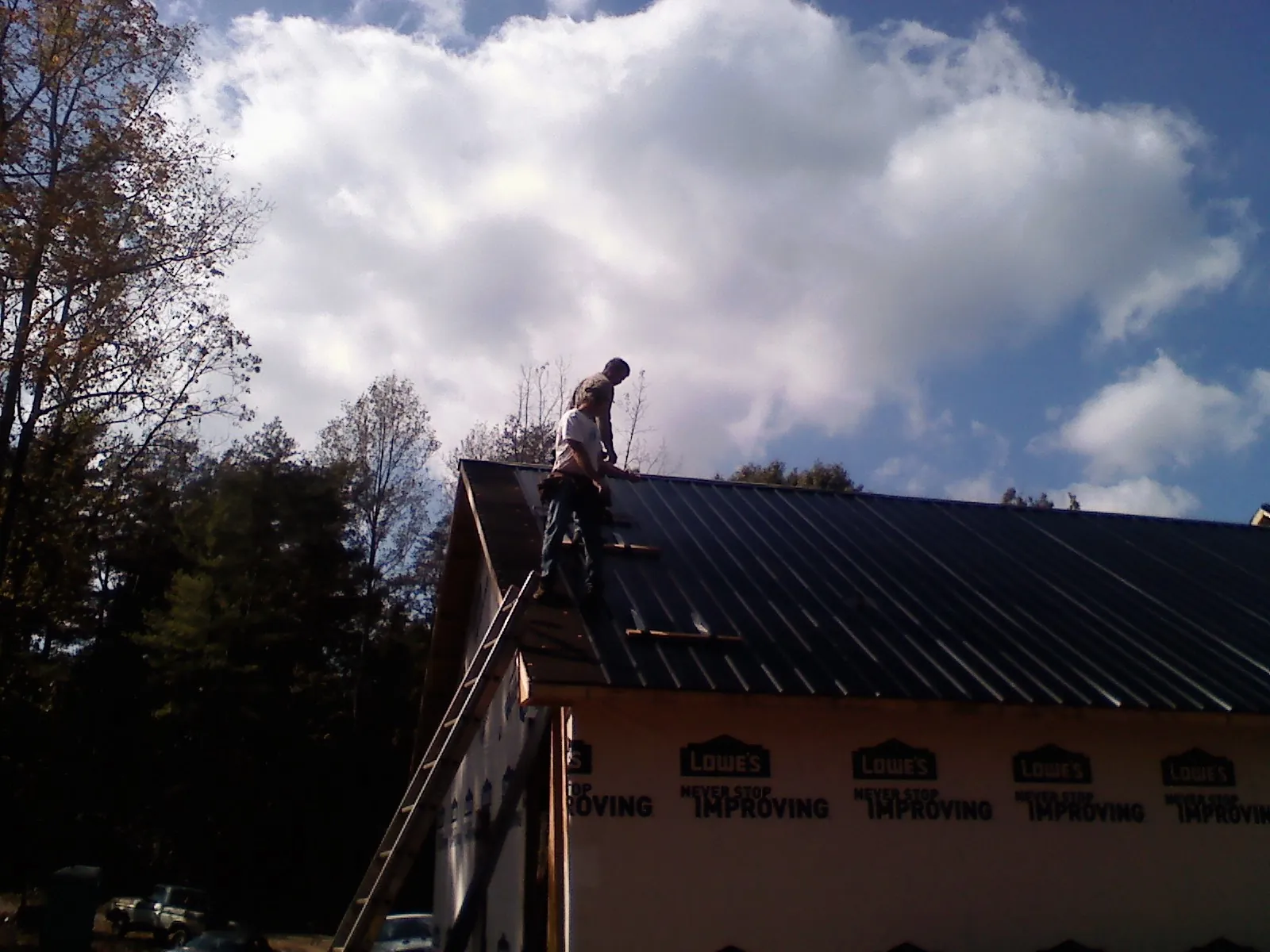 Roofer fastening dark metal panels high against a cloudy sky, from a Roof Inspection job in Interlachen