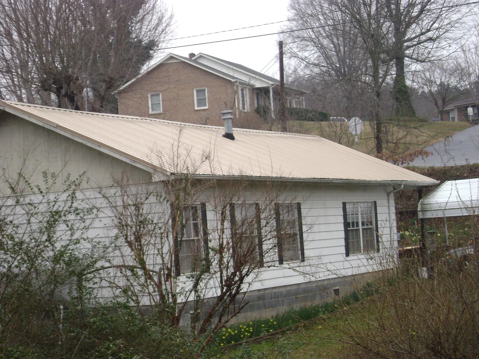 Tan metal roof on a white sided house set into a hillside — Commercial Roofing by Roofing Brothers in Interlachen